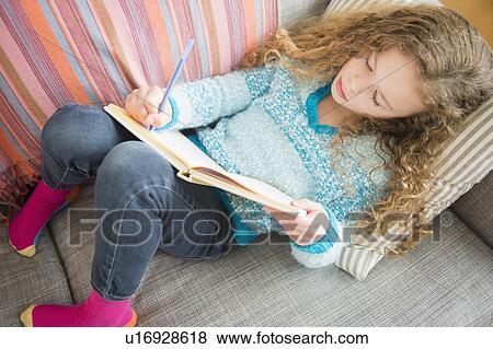 Stock Photo - Girl (10-11) lying on sofa and writing in notebook. Fotosearch