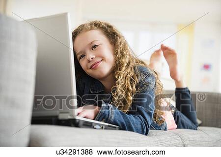 Girl (10-11) with laptop lying on sofa View Large Photo Image Stock Photo - Girl (10-11) with laptop lying on sofa. Fotosearch