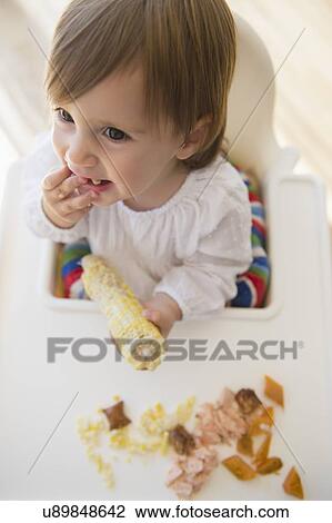 Stock Image - Girl (2-3) eating sweet corn. Fotosearch