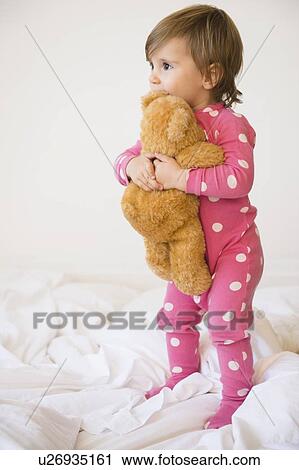 Stock Image - Girl (2-3) embracing teddy bear on bed. Fotosearch