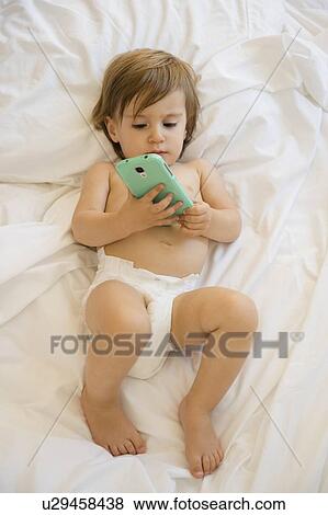 Stock Photo - Girl (2-3) lying on bed and holding smartphone. Fotosearch