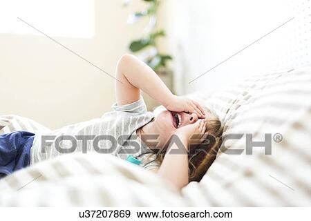 Stock Photo - Girl (4-5) lying on bed with open mouth and covering face. Fotosearch