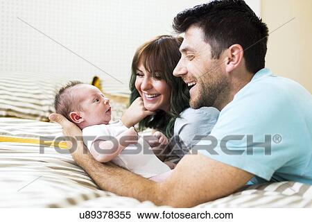 Happy parents playing with baby boy (6-11 months) on bed View Large Photo Image Stock Photography - Happy parents playing with baby boy (6-11 months) on bed. Fotosearch