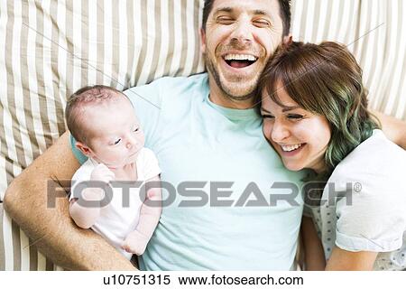 Stock Photography - Happy parents with baby boy (6-11 months) lying on bed. Fotosearch