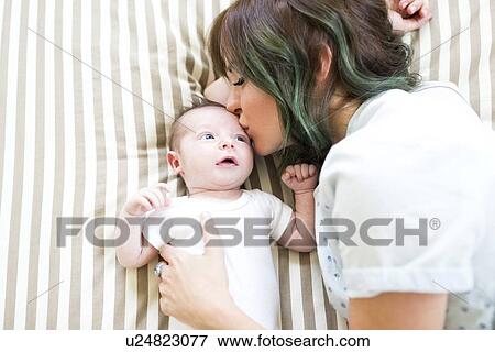 Stock Photo - Mother kissing baby boy (6-11 months) on bad. Fotosearch