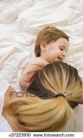 Stock Image - Mother playing with girl (2-3) on bed. Fotosearch