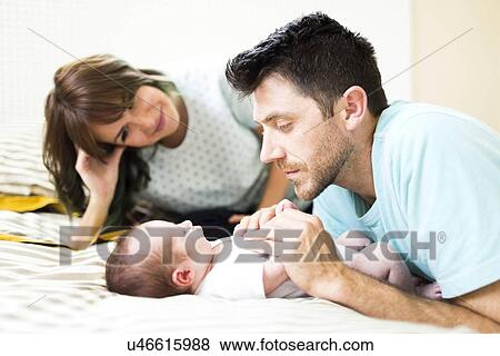 Stock Photo - Parents playing with baby boy (6-11 months) on bed. Fotosearch