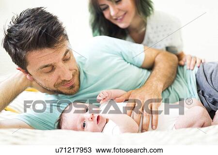 Stock Image - Parents with baby boy (6-11 months) relaxing on bad. Fotosearch