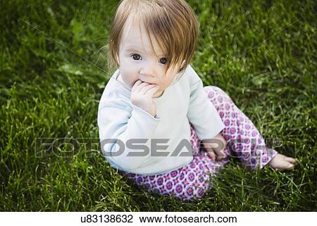 Stock Image - Portrait of baby girl (6-11 months) with hand in mouth. Fotosearch