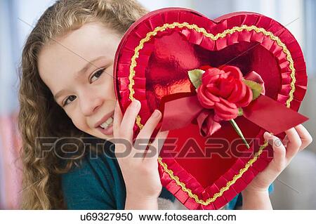Stock Image - Portrait of girl (10-11) with heart-shaped chocolate box. Fotosearch