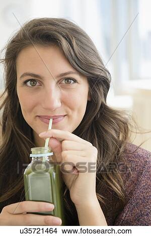 Picture - Portrait of woman drinking juice from bottle with straw. Fotosearch