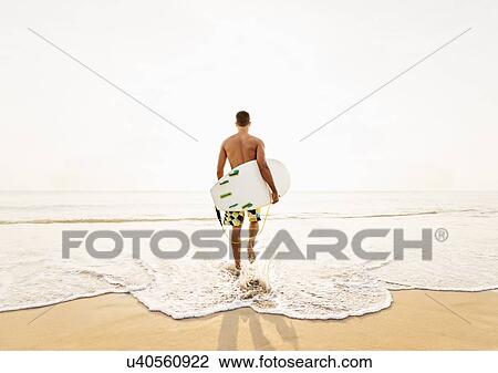 Stock Image - Rear view of surfer on beach. Fotosearch