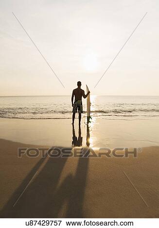 Stock Photo - Rear view of surfer on beach. Fotosearch