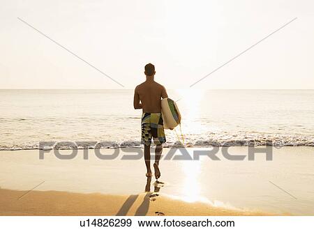 Rear view of surfer walking towards sea at sunset View Large Photo Image Stock Photo - Rear view of surfer walking towards sea at sunset. Fotosearch