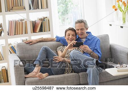 Stock Photo - Senior couple sharing cell phone on sofa. Fotosearch