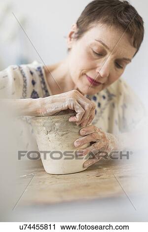 Stock Image - Senior woman making flower pot at workshop. Fotosearch