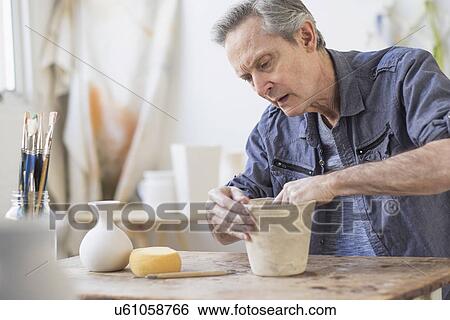 Stock Photograph - Senior woman making flower pot at workshop. Fotosearch