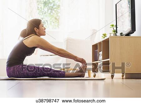 Stock Photo - Side-view of woman exercising in living room. Fotosearch