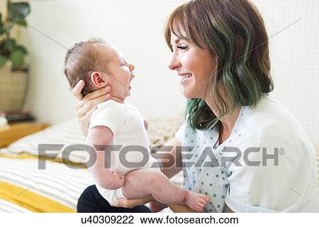 Stock Image - Smiling mother holding baby boy (6-11 months). Fotosearch