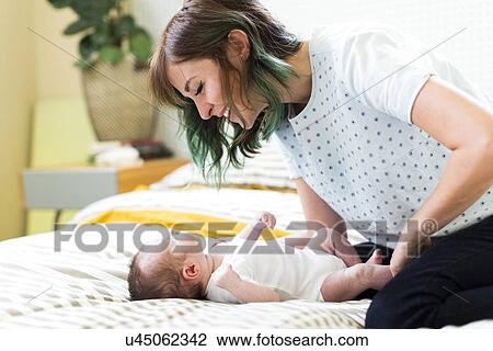Stock Image - Smiling mother playing on bad with baby boy (6-11 months). Fotosearch