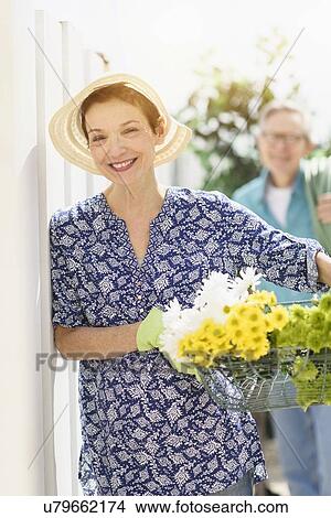 Picture - Smiling senior woman with flowers with senior man in background. Fotosearch