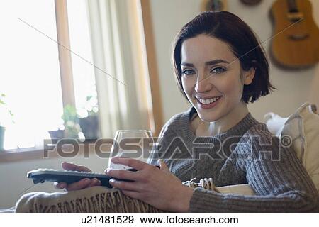 Stock Photo - Woman at home with glass of wine and remote control. Fotosearch