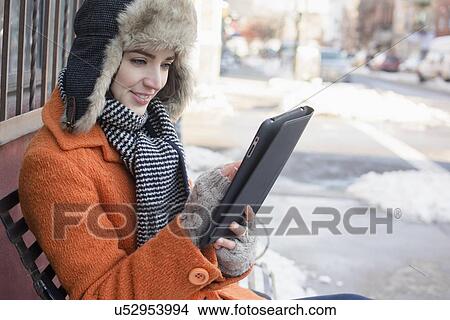 Picture - Woman on bench in street using tablet. Fotosearch