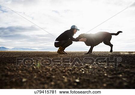 Stock Image - Woman with dog outdoors at sunrise. Fotosearch