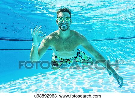 Stock Image - Young man doing ok sign in swimming pool. Fotosearch