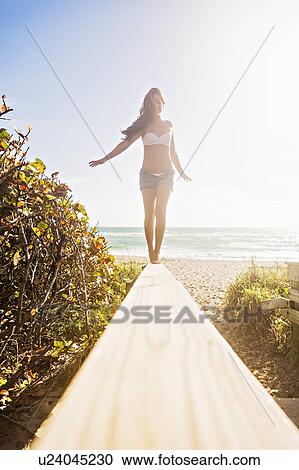 Stock Image - Young woman balancing on boardwalk. Fotosearch