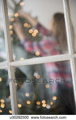 Stock Image - Young woman decorating christmas tree. Fotosearch