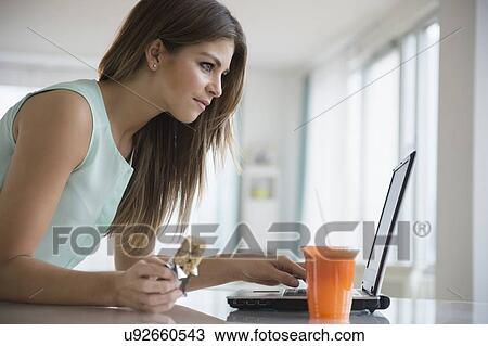 Young woman eating snack while working with laptop View Large Photo Image Stock Image - Young woman eating snack while working with laptop. Fotosearch