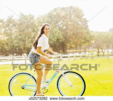 Stock Image - Young woman riding bicycle in park. Fotosearch