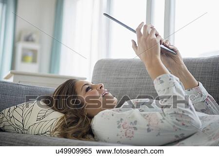 Stock Photography - Young woman with digital tablet lying on sofa. Fotosearch