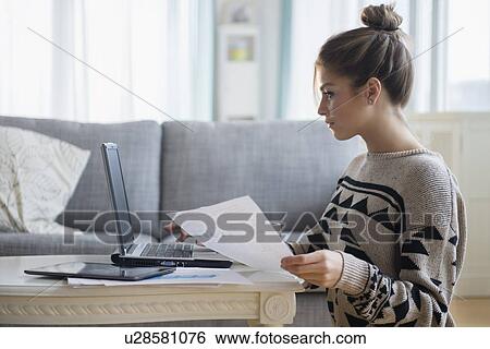 Stock Photograph - Young woman working with laptop in living room. Fotosearch