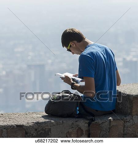 Stock Image - "Man reading a book on wall, San Cristobal Hill, Santiago, Santiago Metropolitan Region, Chile". Fotosearch