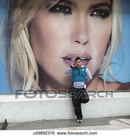 Stock Photograph - "Man talking on phone in front of poster, Santiago, Santiago Metropolitan Region, Chile". Fotosearch