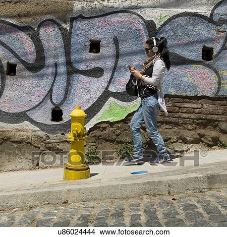 Picture - "Woman listening to music with headphones on street, Valparaiso, Chile". Fotosearch