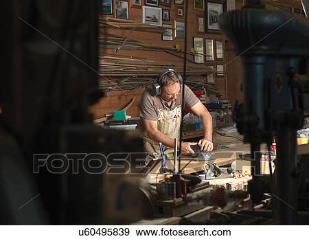 Stock Photo - Boat builder sanding wood in workshop. Fotosearch