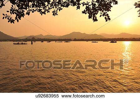 Stock Photography - "Boats on lake at sunset, Hangzhou, China". Fotosearch
