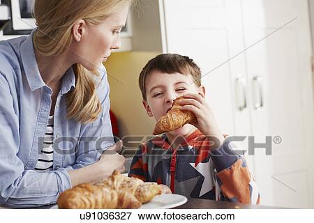 Stock Photo - "Boy biting croissant, mother watching". Fotosearch