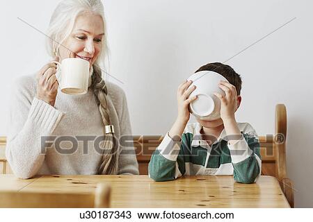 Stock Image - Boy drinking milk from bowl with grandmother. Fotosearch
