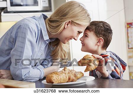 Stock Photo - "Boy holding croissant, face to face with mother". Fotosearch