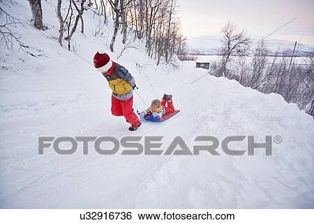 Stock Photograph - "Boy pulling brother on toboggan up snow covered hill, Hemavan, Sweden". Fotosearch