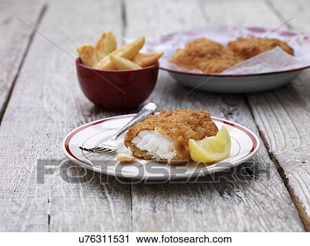 Stock Image - Breaded chunky cod with bowl of french fries on wooden table. Fotosearch