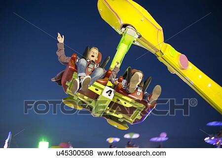 Stock Photo - Brother and sister mid air on fairground ride at night. Fotosearch
