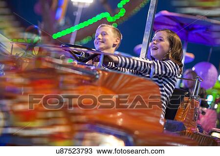 Stock Image - Brother and sister on fairground ride at night. Fotosearch