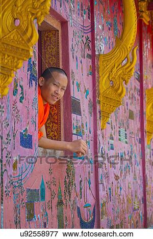 Stock Photo - "Buddhist monk looking out of Wat Xieng Thong window, Luang Prabang, Laos". Fotosearch