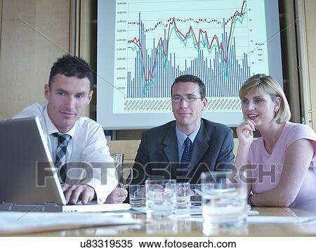Business colleagues looking at laptop in front of screen in meeting View Large Photo Image Stock Photography - Business colleagues looking at laptop in front of screen in meeting. Fotosearch