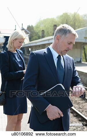 Stock Image - Businessman and woman checking watch on railway platform. Fotosearch